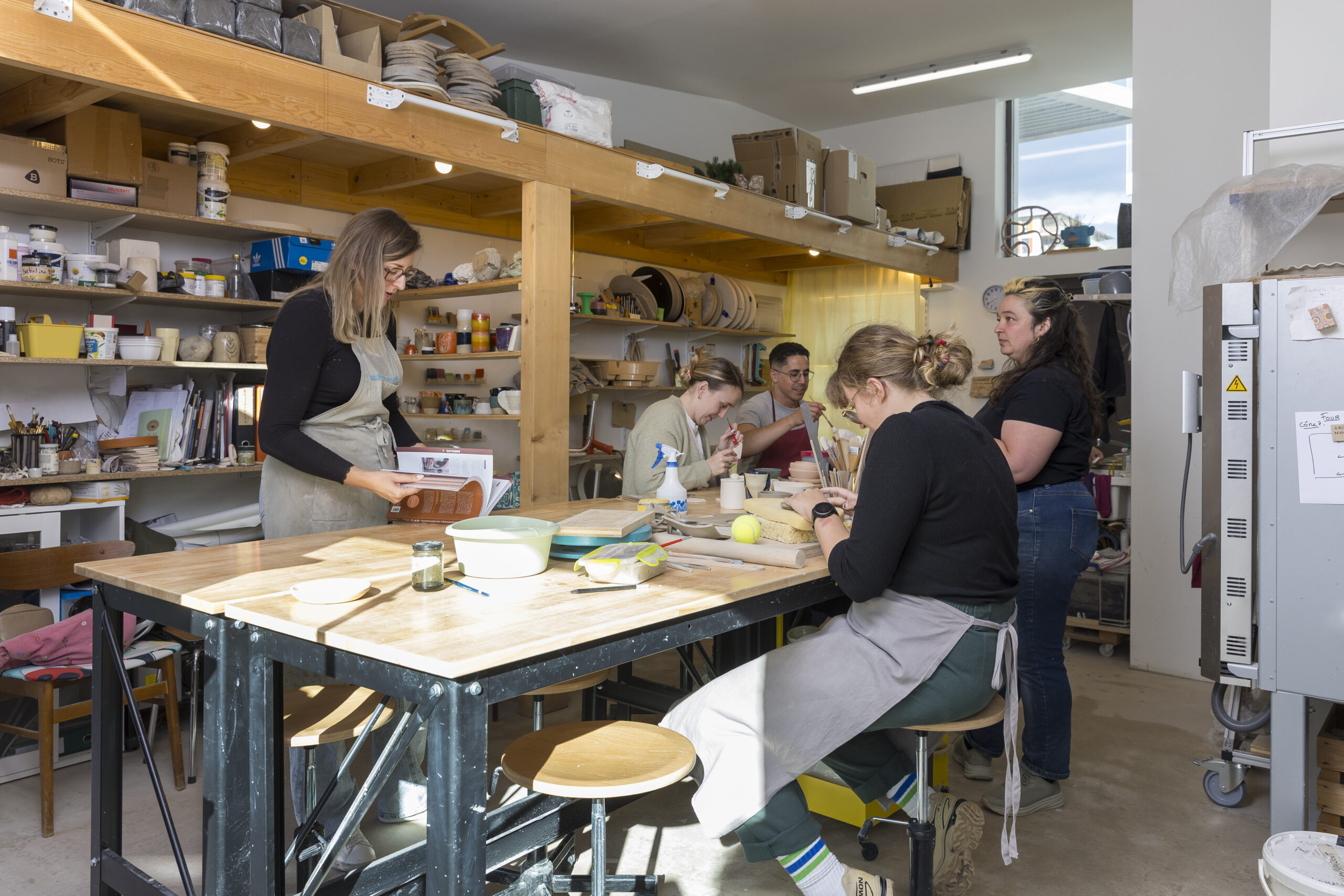 Photographie de l'intérieur de l'atelier ou quatre élèves et l'enseignante travaillent autour des tables.